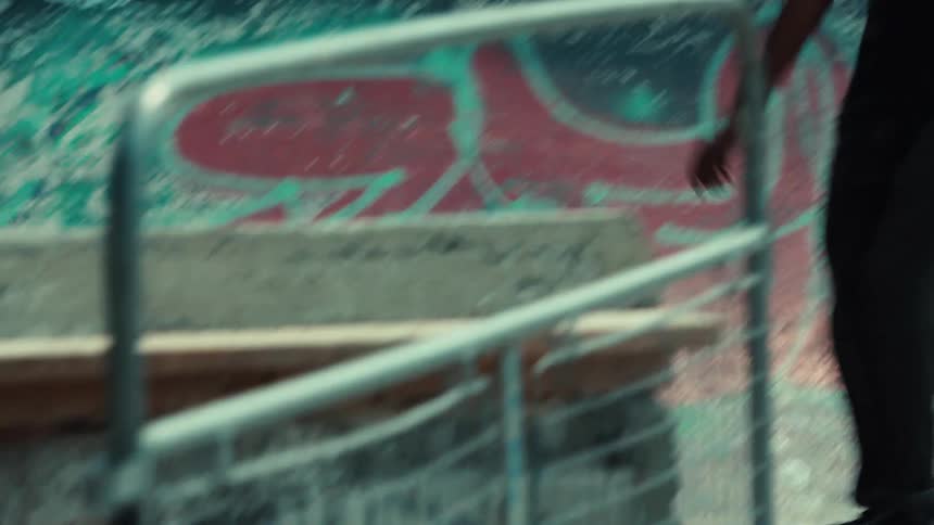 A dynamic low-angle tracking shot follows a skateboarder's feet as they cruise through a concrete, graffiti-covered skatepark