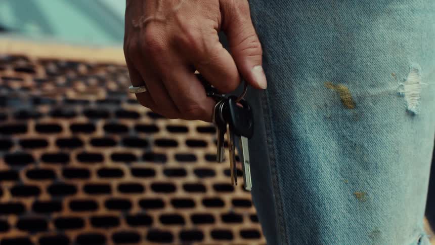 A close-up shot shows a hand fidgeting with a set of car keys against a backdrop of ripped and stained blue jeans