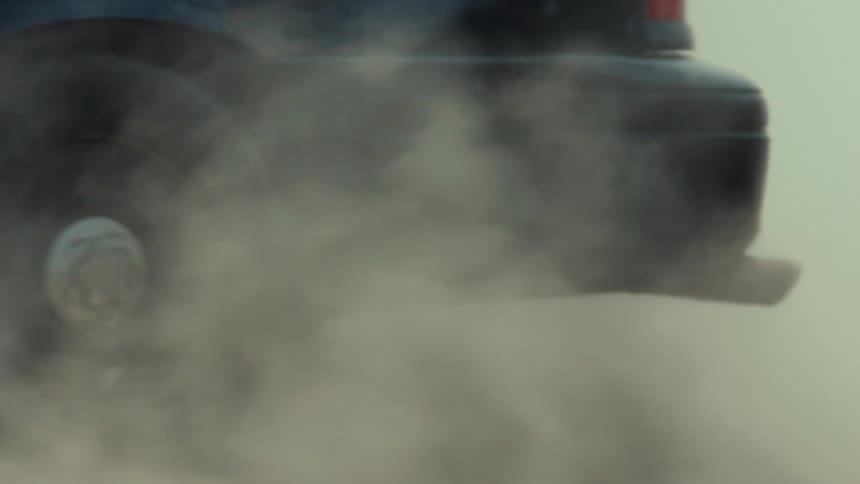 Close up slow motion shot of a car kicking up a cloud of dust while speeding down a dirt road
