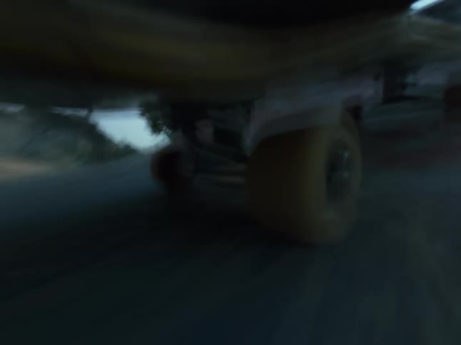 A dynamic low-angle point-of-view shot follows the wheels of a skateboard as it speeds along the pavement of a skatepark