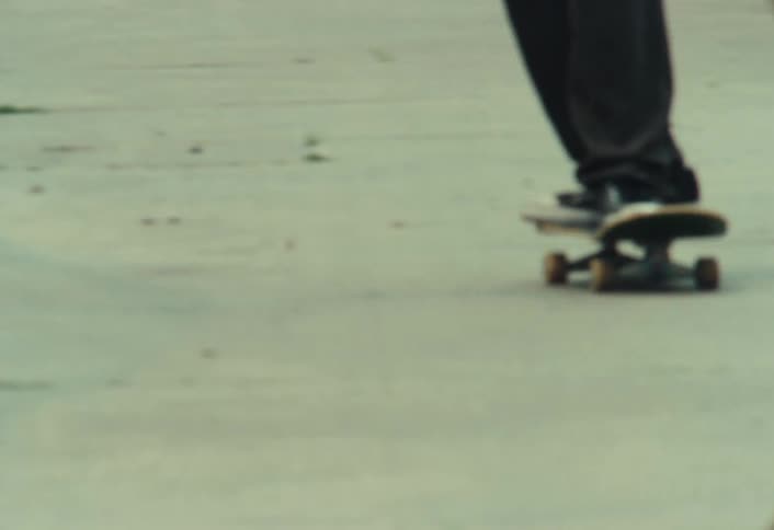 Slow motion shot of a skater with a backpack cruising down a gritty urban alley and ollieing over a traffic cone
