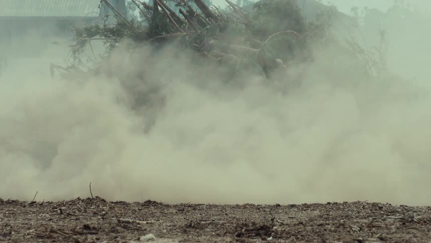 A race car speeds down a dirt track in slow motion, kicking up a massive cloud of dust as other cars follow behind