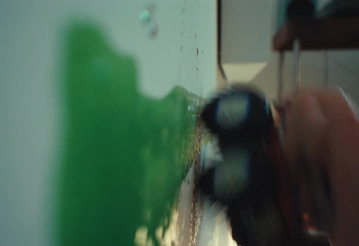 A child playfully drives a toy monster truck through green paint, leaving tire tracks on a white wall in this vertical video