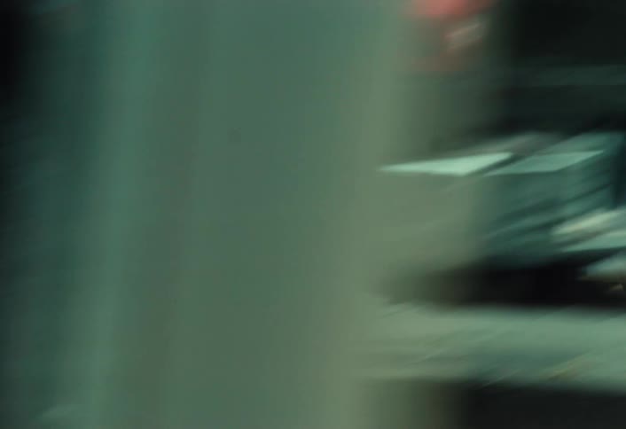 A tracking shot follows a young man with a red backpack as he skateboards down a city sidewalk, carrying a plastic jug