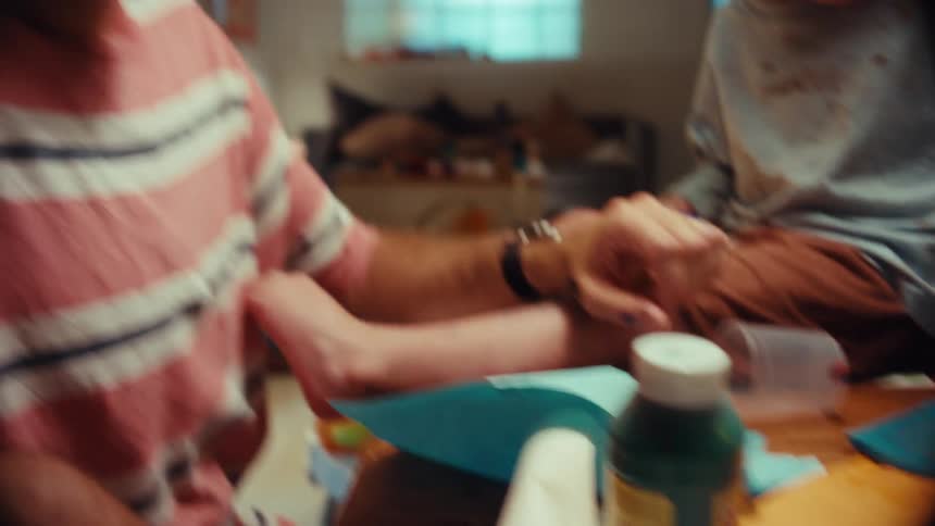 A father and his young child enjoy a messy and creative painting session at home, with the camera revealing the dad has paint on his face