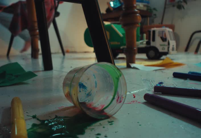 A close-up shot of a spilled cup of paint on a messy floor surrounded by markers and toys after a child's arts and crafts session