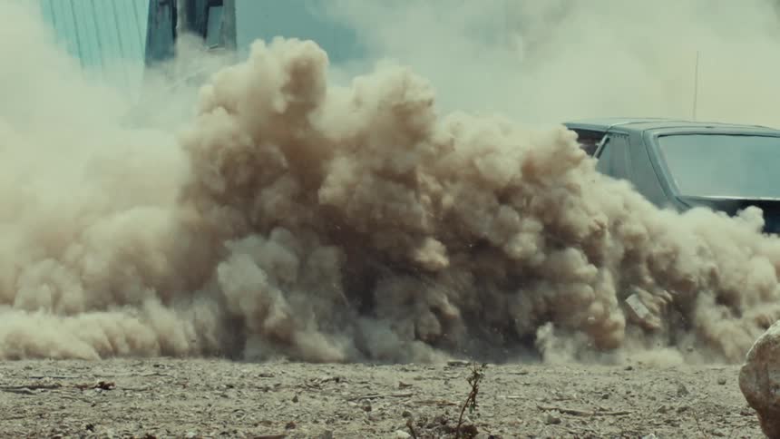 A car's spinning wheels kick up a massive cloud of dust from a dirt road in super slow motion