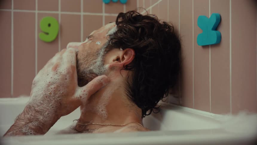 A person gently and lovingly washes a man's hair and face while he relaxes in a soapy bubble bath