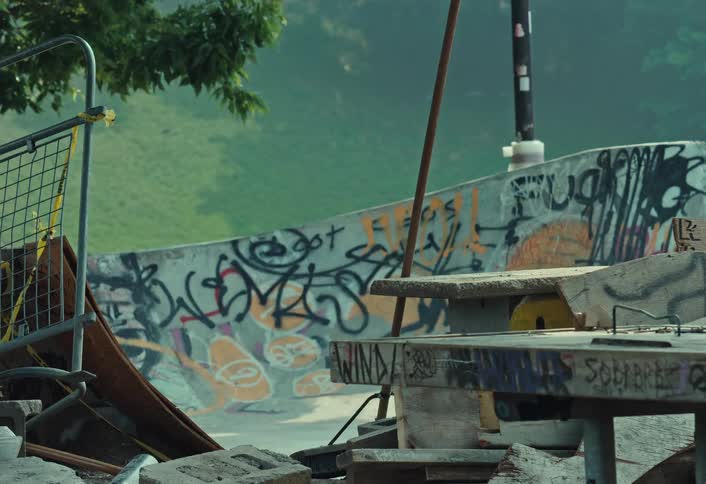 A static, gritty shot of a neglected urban skatepark covered in graffiti with rubble in the foreground