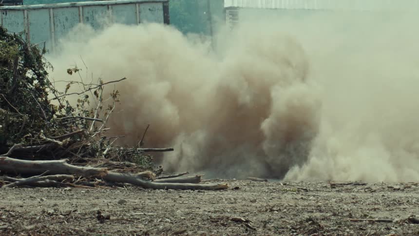 A ground-level slow-motion view of a powerful explosion that kicks up a massive cloud of dust and debris
