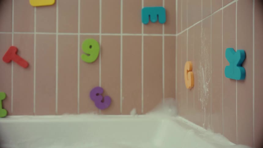 A bearded man experiences an emotional moment in a bubble bath, rinsing his face in slow motion in a bathroom with children's toys on the wall