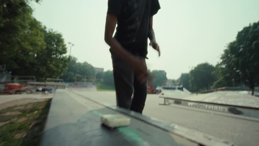 A cool skateboarder waxes a skate ledge with a block of wax at an urban skatepark on a sunny day