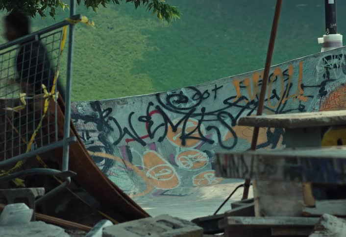 A lone skateboarder glides through a gritty, graffiti-covered skatepark with debris in the foreground