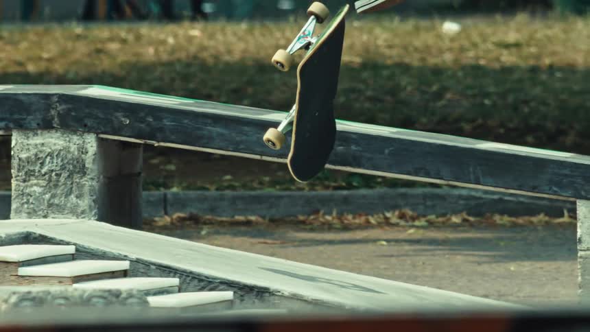 A skateboarder executes a kickflip to grind down a rail in super slow motion at a skatepark