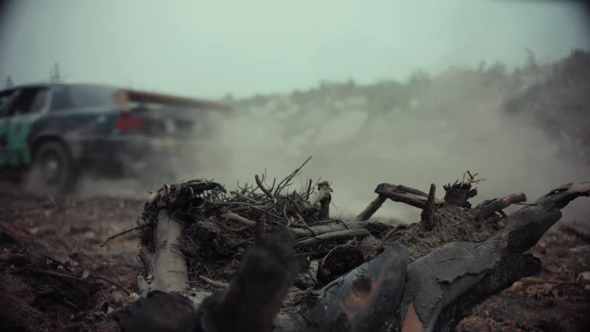 A gritty slow-motion shot of a modified race car kicking up dust as it speeds through a desolate, post-apocalyptic landscape