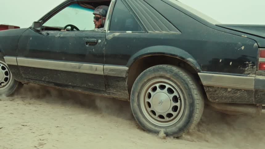 A slow motion shot starts on the spinning tire of a black muscle car doing a burnout and pulls back to reveal the driver