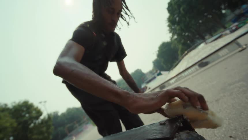 Skateboarder in slow motion meticulously waxes a metal ledge at the skatepark