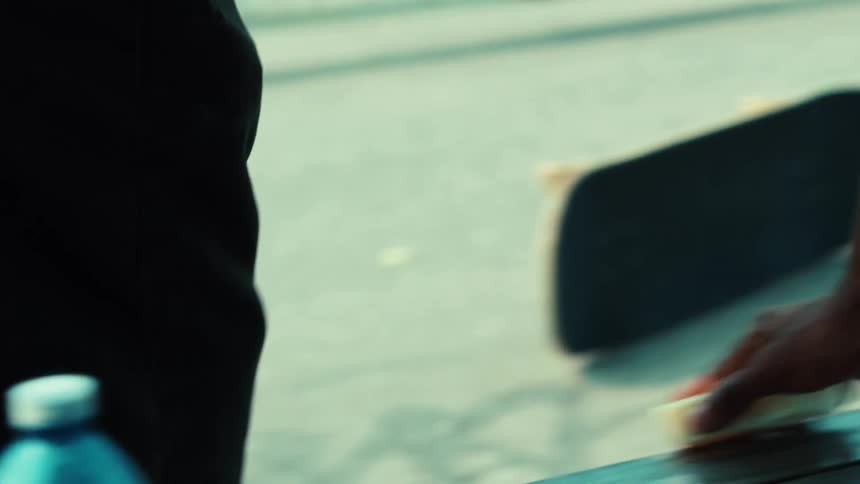 A skateboarder waxes a metal rail with a block of wax at a skatepark in slow motion