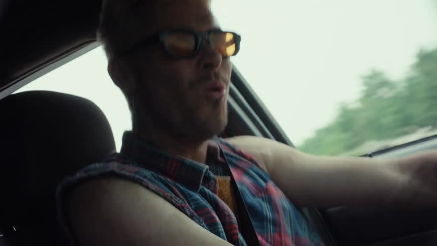 Stylish man with bleached hair and sunglasses sings and dances while driving his car