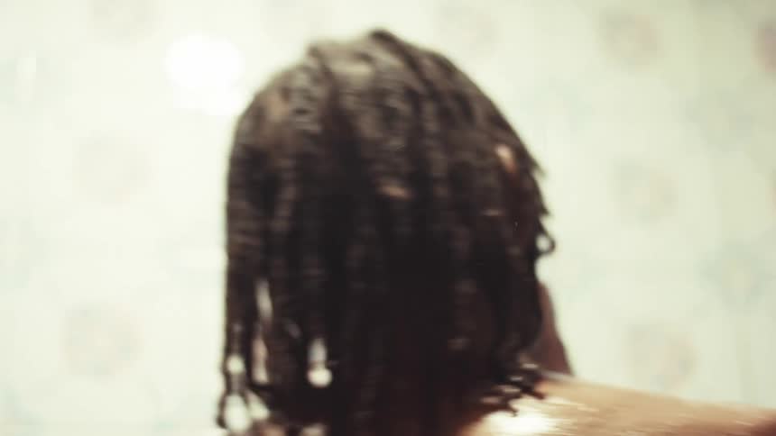 A close-up slow-motion shot captures a person with dreadlocks washing their soapy back and shoulders in the shower