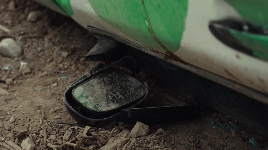 A wrecked car's broken and dirty side mirror lies on the dusty ground after an accident