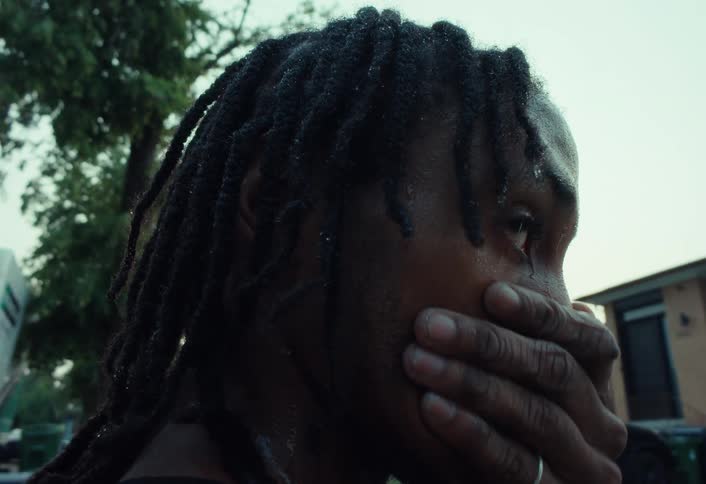 An emotional slow-motion close-up of a distressed young man with dreadlocks crying in the rain