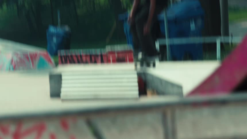 A skateboarder in slow motion performs a flip trick over a set of stairs at an outdoor skatepark