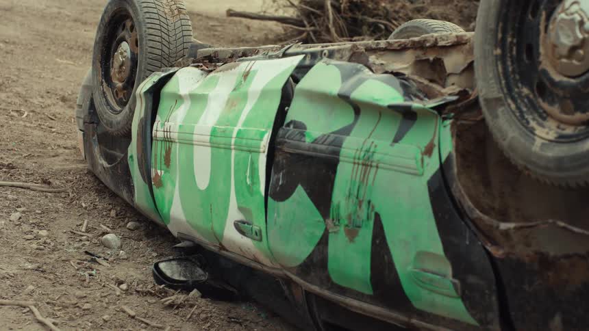 Close up of a destroyed and abandoned car flipped on its side on a dirt road
