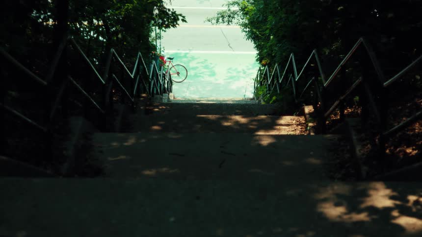 From the top of a shady staircase, a person skateboards past a bike on a bright green bike lane