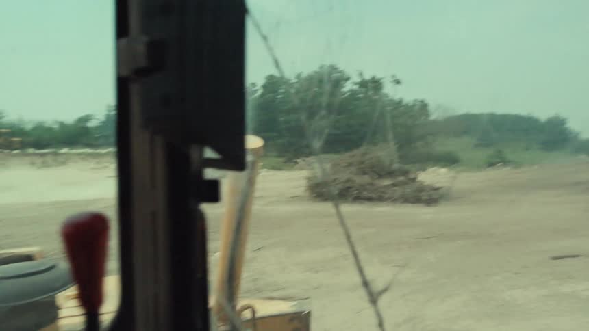 From the cracked windshield of a bulldozer, a vintage car performs a dusty drift in a rural junkyard