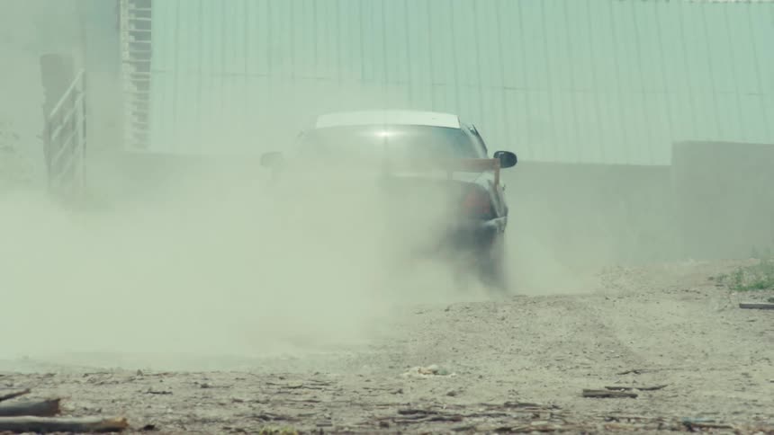 A modified race car does a burnout on a dirt road, disappearing into a thick cloud of smoke and dust