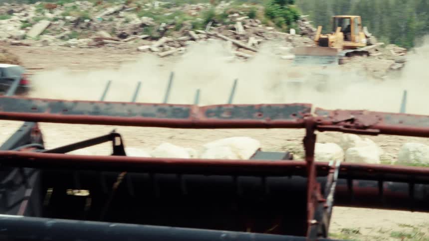 A demolition derby car speeds through a dusty rural junkyard before crashing in slow motion