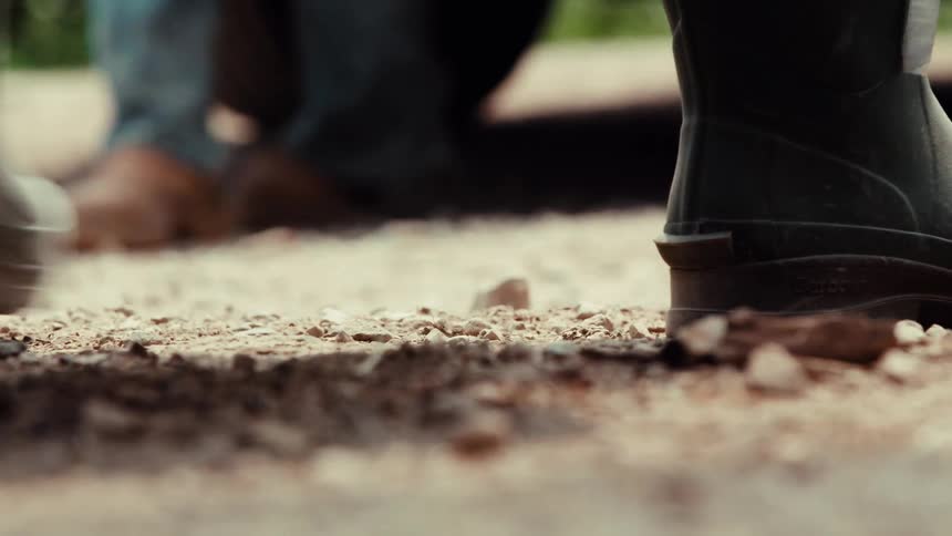 A low-angle close-up of a person's green Wellington boots walking on a dusty rural path