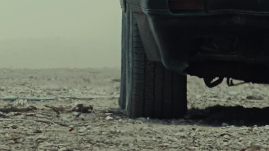 The back tire of a car sits flat on the dusty ground of a desolate desert