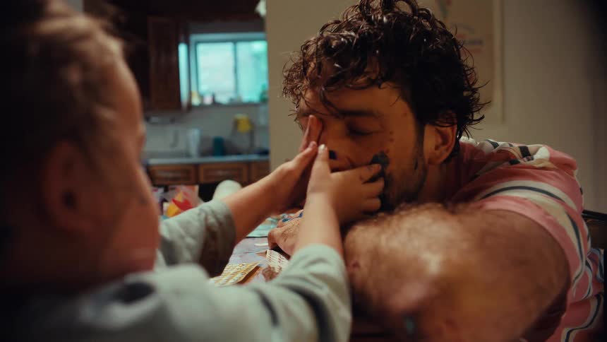 A young girl playfully paints on her tired but patient father's face during a messy craft session at home