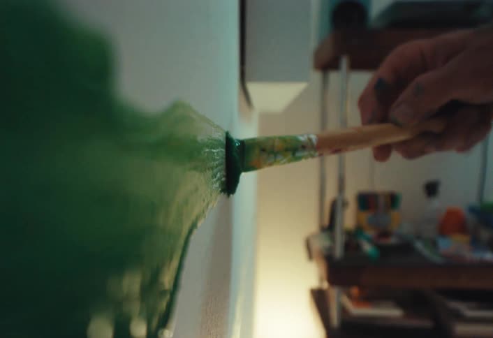 Macro shot of a paintbrush applying a thick, dripping green stroke onto a white wall