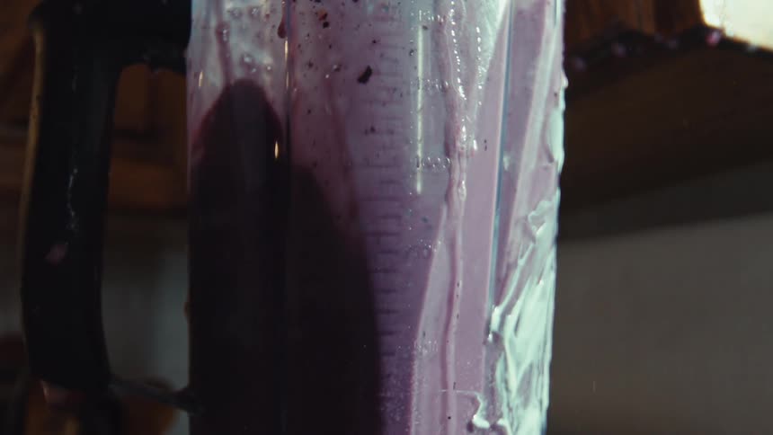 A messy blender splatters purple and white smoothie everywhere in a dramatic slow-motion close-up