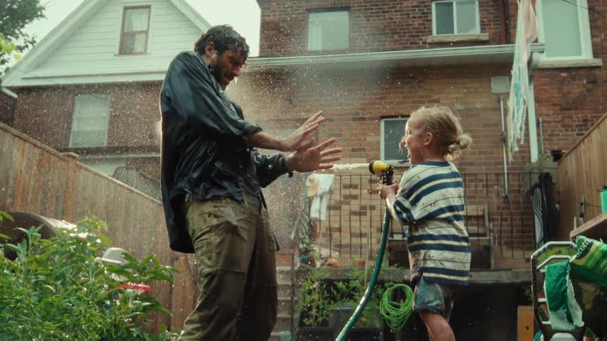 Slow motion shot of a happy toddler playfully spraying their father with a water hose in the backyard