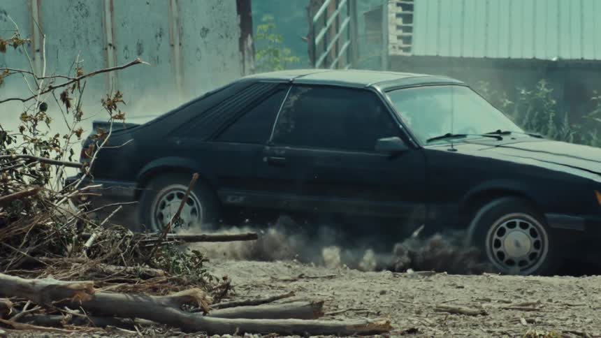 Slow motion shot of a black muscle car spinning its tires on a gravel road, creating a cloud of dust