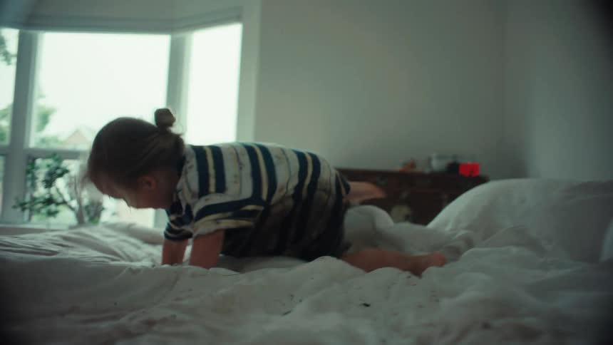 A muddy little boy with boundless energy happily jumps all over clean white bedsheets in a bedroom