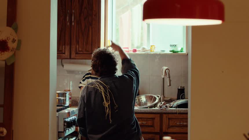 A playful father and his laughing child have fun cooking spaghetti together in a sunlit kitchen