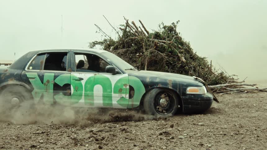 A post-apocalyptic style car performs an aggressive burnout in slow motion, kicking up a massive cloud of dust in a junkyard