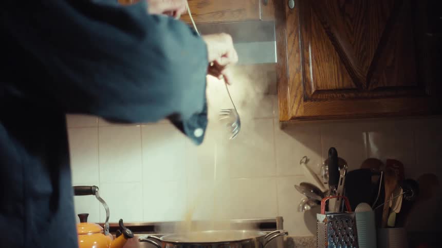 A loving father playfully shares a single spaghetti noodle with his son while cooking dinner in their home kitchen