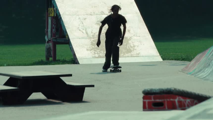 Slow motion footage shows a skilled skateboarder gliding up and down a ramp at a skatepark before launching into a stylish kickflip