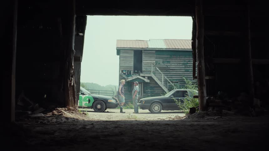 Two men argue and fight next to their cars at a rural farm before speeding off in a cloud of dust