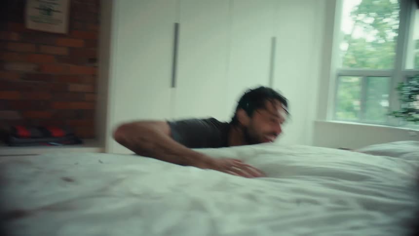 A dirty and happy father playfully chases his child across the bed in a modern bedroom on a rainy day