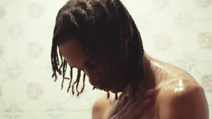 Close-up slow motion shot of a Black man with dreadlocks thoughtfully washing his body in the shower