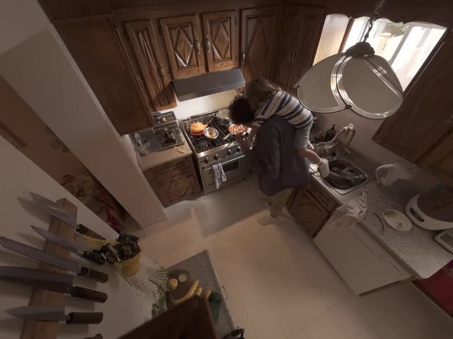 From a high wide-angle perspective, a loving father multitasks by cooking at the stove with his toddler riding piggyback in their home kitchen
