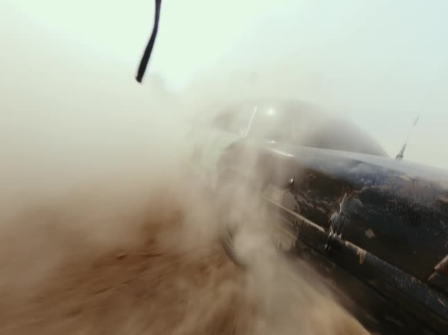 A seamless loop of a demolition derby car kicking up a massive cloud of dust while racing on a dirt track in slow motion