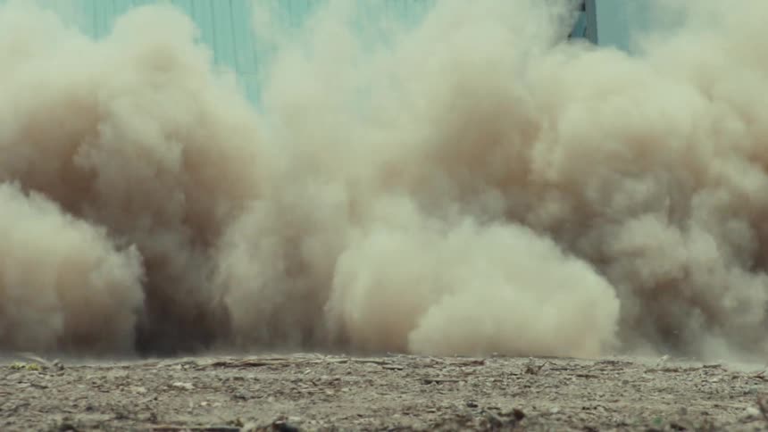 A black muscle car speeds down a dirt road, kicking up a massive cloud of dust in slow motion